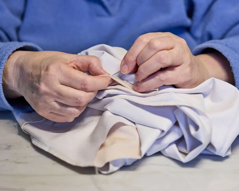 Manos cosiendo a mano el borde de una prenda blanca